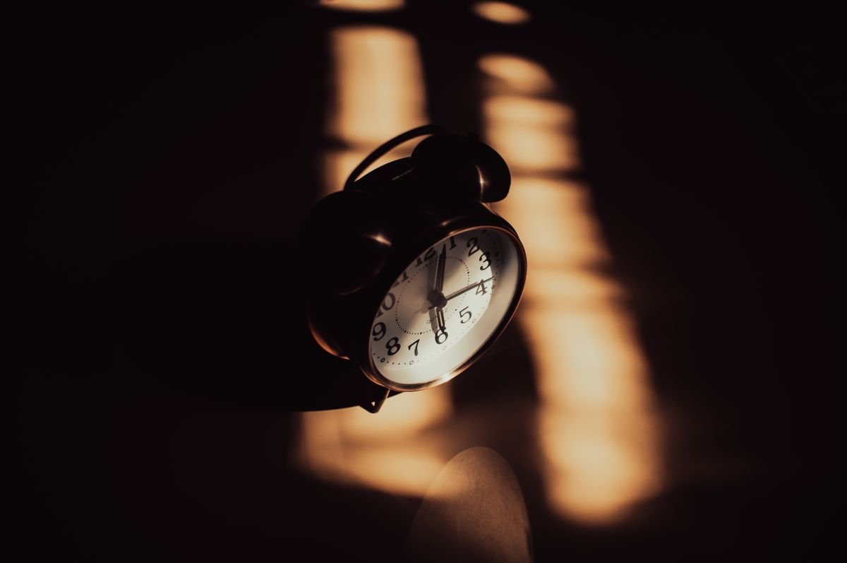 Analog alarm clock in moody night-time shadows — cluster headache attacks run on a schedule