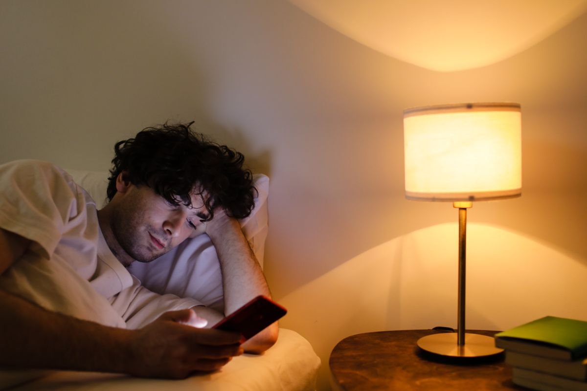 Man in bed searching his phone by lamplight — where most frenulum tear questions start